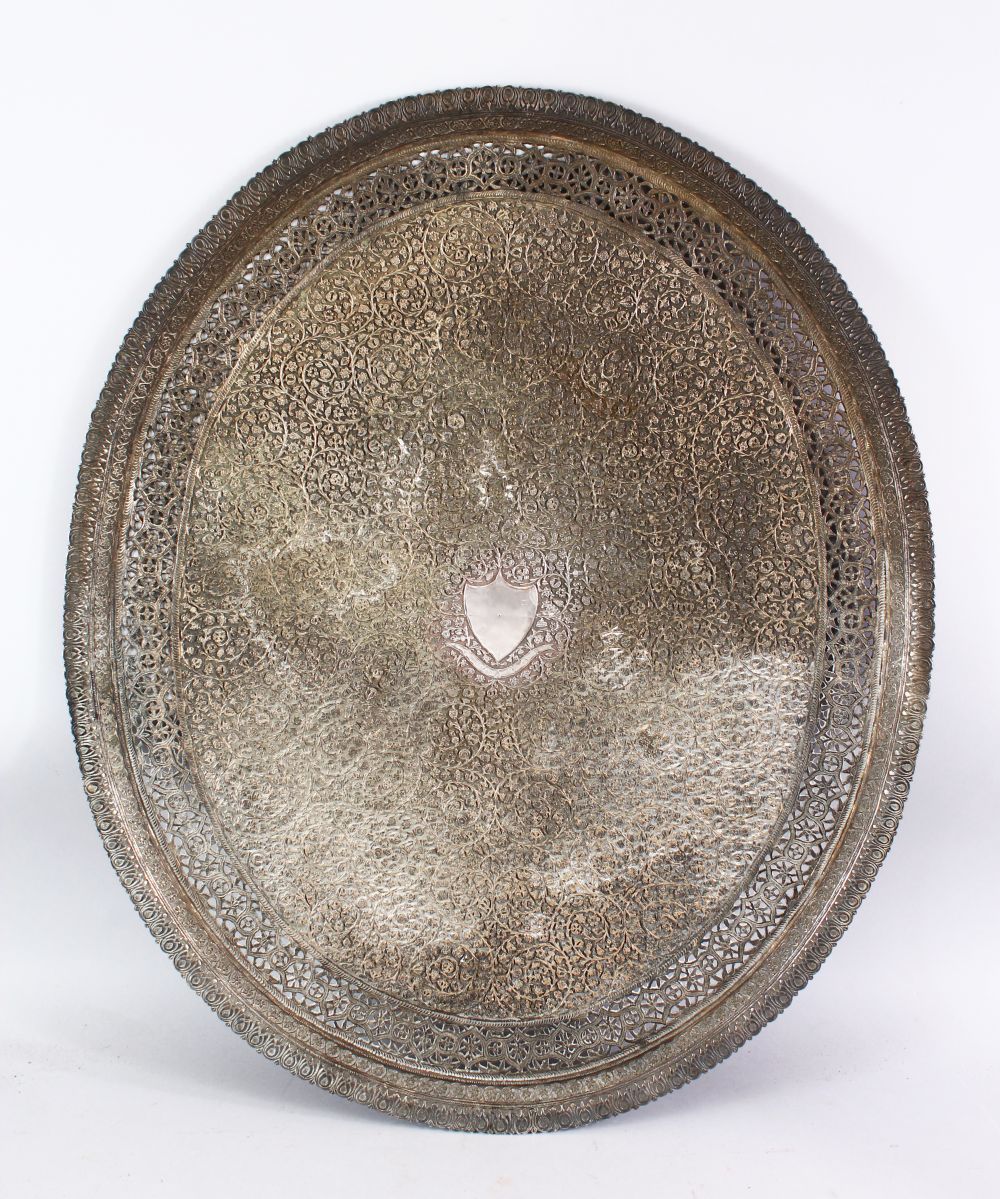 A LARGE INDIAN SILVERED BRONZE OR BRASS TRAY, with a central crest and scrolling foliate, 68.5cm x