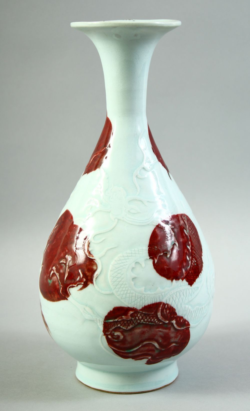 A CHINESE UNDER GLAZED RED AND WHITE DRAGON VASE, the body carved with a dragon and stylised flames,