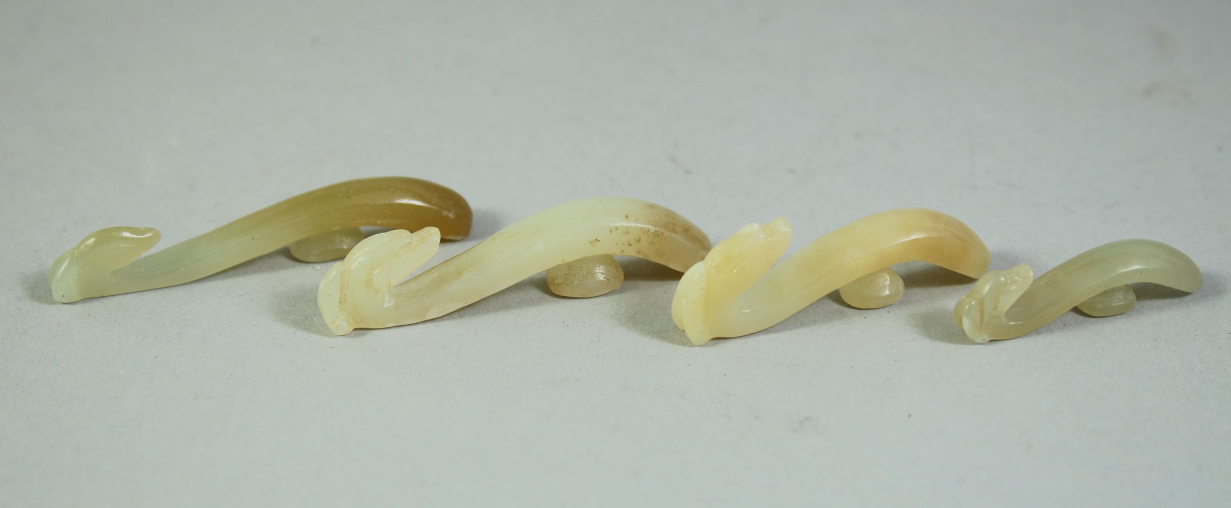 FOUR SMALL CHINESE CARVED JADE HOOKS, (4).