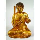 A GILT BRONZE MODEL OF A SEATED DEITY, sitting with legs crossed holding a sword in one hand and