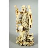 A JAPANESE CARVED IVORY OKIMONO GROUP, depicting a standing priest with another priest at his