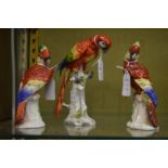 A Naples porcelain model of a parrot on a tree stump together with a pair of similar parrots.