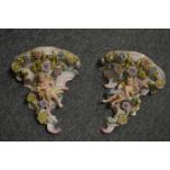 A Capodimonte style pair of porcelain wall brackets with floral encrusted and cherub decoration.