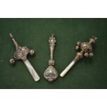 Three silver rattles, two with mother-of-pearl handles and bells.