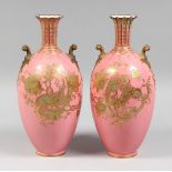 A PAIR OF ROYAL CROWN DERBY PINK GROUND TWO HANDLED VASES with gilt decoration 11.5ins high.