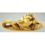 A JAPANESE CARVED IVORY NETSUKE of a seated deity on the back of a giant fish, signed to the base,