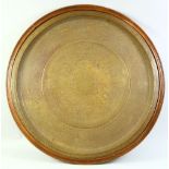 A LARGE ISLAMIC BRASS DISH WITH KUFIC SCRIPT, mounted to a wooden backing, overall 75cm diameter.