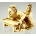 A JAPANESE CARVED IVORY NETSUKE of a man leaning on a table; his back being massaged by a young