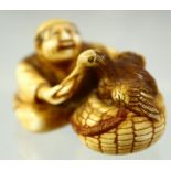 A JAPANESE CARVED IVORY NETSUKE of a seated man hand feeding a bird in a basket, signed to the base,
