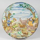 A LARGE ITALIAN FAIENCE CIRCULAR CHARGER as a man playing pipes, three girls and goats.