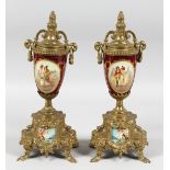 A PAIR OF 19TH CENTURY GILT METAL AND PORCELAIN URNS painted with figures with pineapple finials and