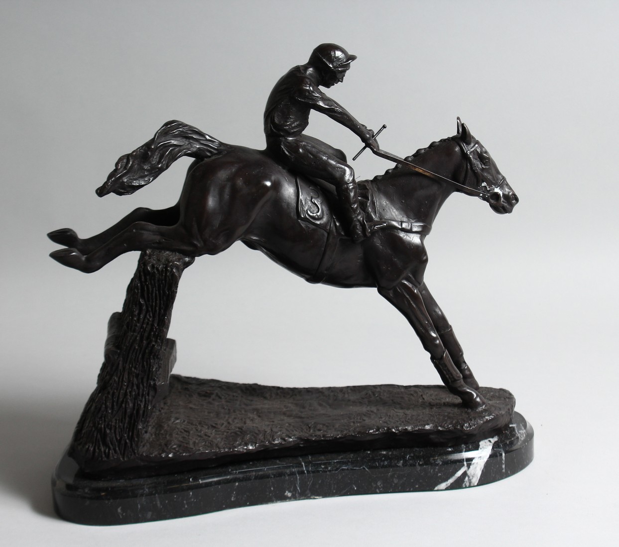 A BRONZE HORSE AND JOCKEY over the sticks, on a marble base.