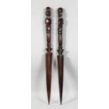 A PAIR OF AFRICAN CARVED WOOD DAGGERS. 24ins long.