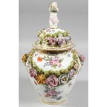 A DRESDEN FLOWER ENCRUSTED VASE AND COVER painted with flowers, with cupid finial. Mark in blue.