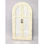 AN UNUSUAL CREAM PAINTED ARCH SHAPED MIRROR with folding doors. 3ft 4ins x 1ft 9ins wide.