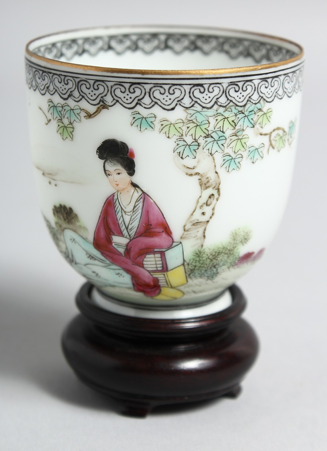 A CHINESE EGGSHELL PORCELAIN CUP AND HARDWOOD STAND, the cup painted with a female figure seated