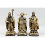 THREE CHINESE GILT BRONZE IMMORTAL FIGURES, each carrying a different object, 30cm, 28.5cm and 28.
