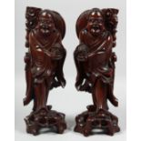 A PAIR OF CHINESE CARVED HARDWOOD FIGURES, raised on pierced hardwood bases, each with inset eyes,