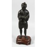 A JAPANESE MEIJI PERIOD BRONZE FIGURE of a man holding a pipe, mounted on a carved hardwood base,