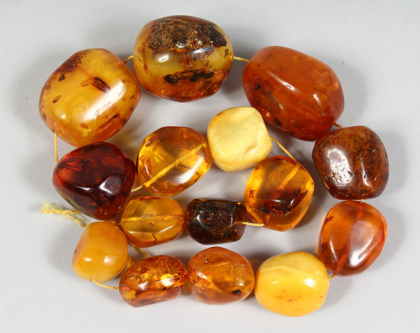 A STRING OF LARGE AMBER TYPE NATURALISTIC BEADS, various shapes and sixes, comprising 15 beads.