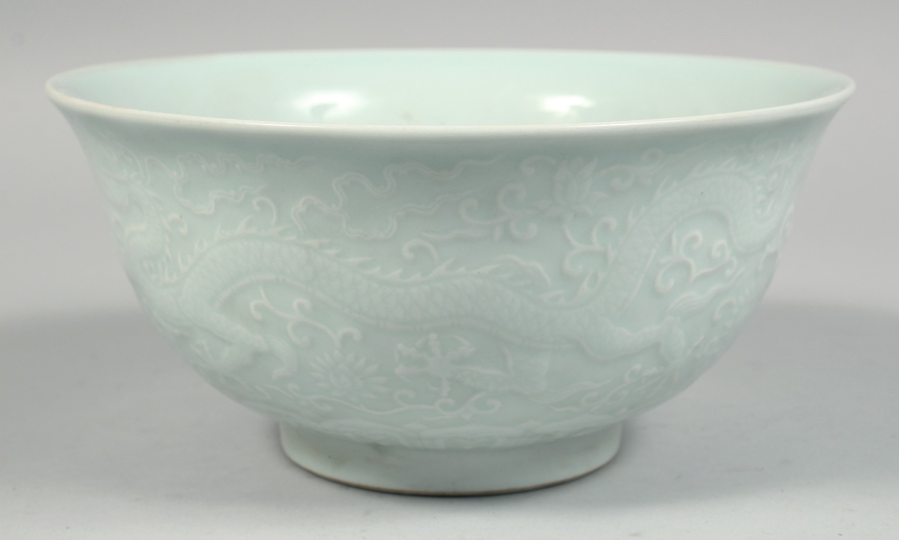 A CHINESE PALE CELADON PORCELAIN BOWL, the exterior with raised decoration depicting dragons and