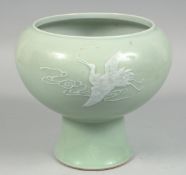 A LARGE CHINESE CELADON PEDESTAL BOWL with raised decoration depicting flying cranes amongst clouds,