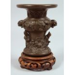 A SMALL JAPANESE BRONZE VASE with hardwood stand, the vase relief cast with figures and twin lion