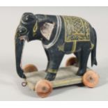 A CARVED INDIAN WOODEN TOY ELEPHANT ON WHEELS, 18cm long.