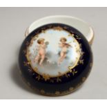 A SMALL BERLIN CIRCULAR BOX AND COVER, blue ground painted with cupids. 3.25ins diameter.