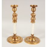 A PAIR OF ROCK CRYSTAL AND GILT METAL EGYPTIAN DESIGN CANDLESTICKS on circular bases. 11.5ins high.