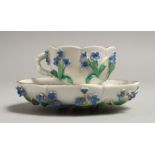 AN AUGUSTUS REX FLOWER ENCRUSTED CUP AND SAUCER. Mark 'A R' in blue.