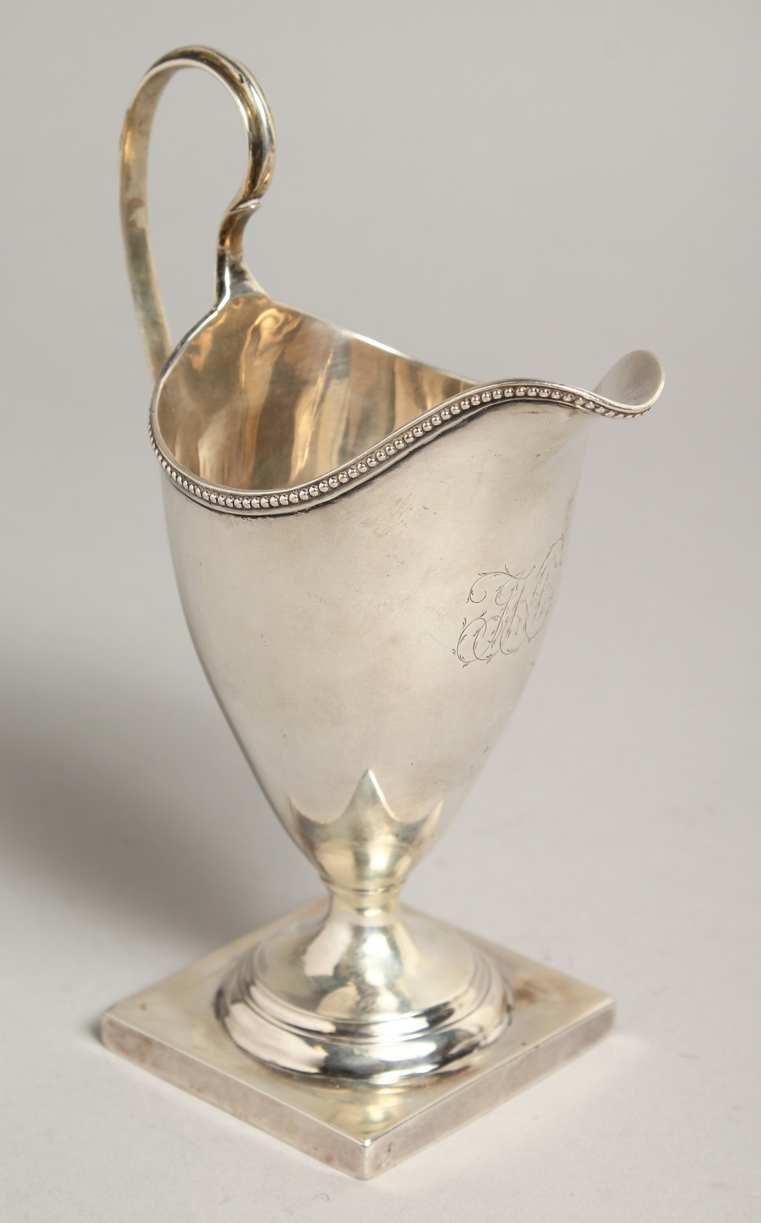 A GEORGE III SILVER HELMET SHAPED CREAM JUG, bead and edge on a square base. London 1784, Maker: