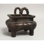 A CHINESE BRONZE SQUARE CENSER with rope handles on four curving legs, the sides with calligraphy.