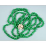 A STRING OF JADE BEADS, triple row with gold, ruby and diamond clasp.
