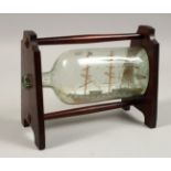 A SHIP IN A BOTTLE on a mahogany stand.