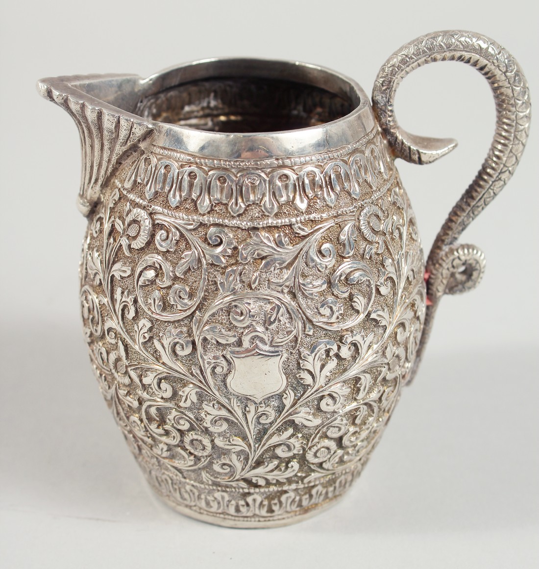 AN INDIAN WHITE METAL ENGRAVED AND CHASED CREAM JUG, with scrolling foliate decoration. 9.5cm high.