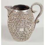 AN INDIAN WHITE METAL ENGRAVED AND CHASED CREAM JUG, with scrolling foliate decoration. 9.5cm high.