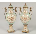 A GOOD PAIR OF FRENCH STYLE PORCELAIN AND METAL URNS AND COVERS with cupid handles. 1ft 8ins high.