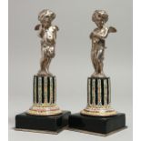 A VERY GOOD PAIR OF SILVERED METAL WINGED CUPIDS standing on an enamel plinth and square base.