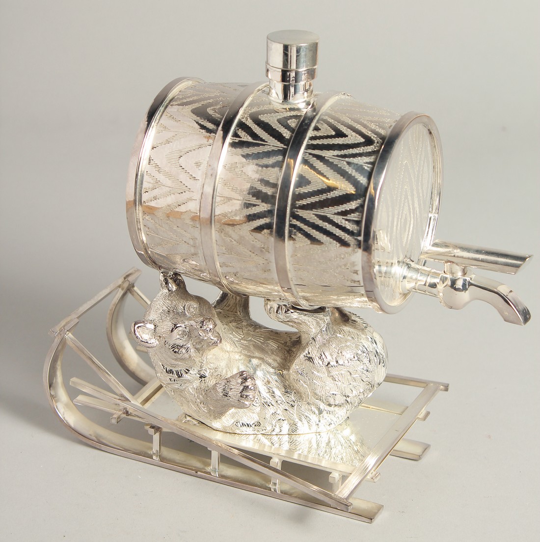 A SILVER PLATED BARREL being held by a bear on a sleigh.