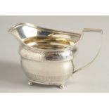 A GEORGE III SILVER CREAM JUG with two bands of atheneum banding, supported on four ball feet.