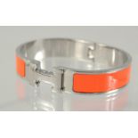 A HERMES ORANGE AND CHROME BANGLE.