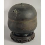 AN EARLY BRONZE LIDDED JAR, together with a carved hardwood stand. Jar 16cm high (including cover)