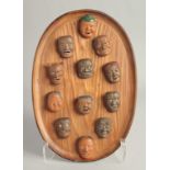 A GOOD COLLECTION OF JAPANESE TERRACOTTA MINIATURE NOH MASKS mounted to an oval wooden plaque, the