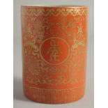 A CHINESE CORAL RED PORCELAIN BRUSH POT, with gilt floral decoration and characters to the exterior,