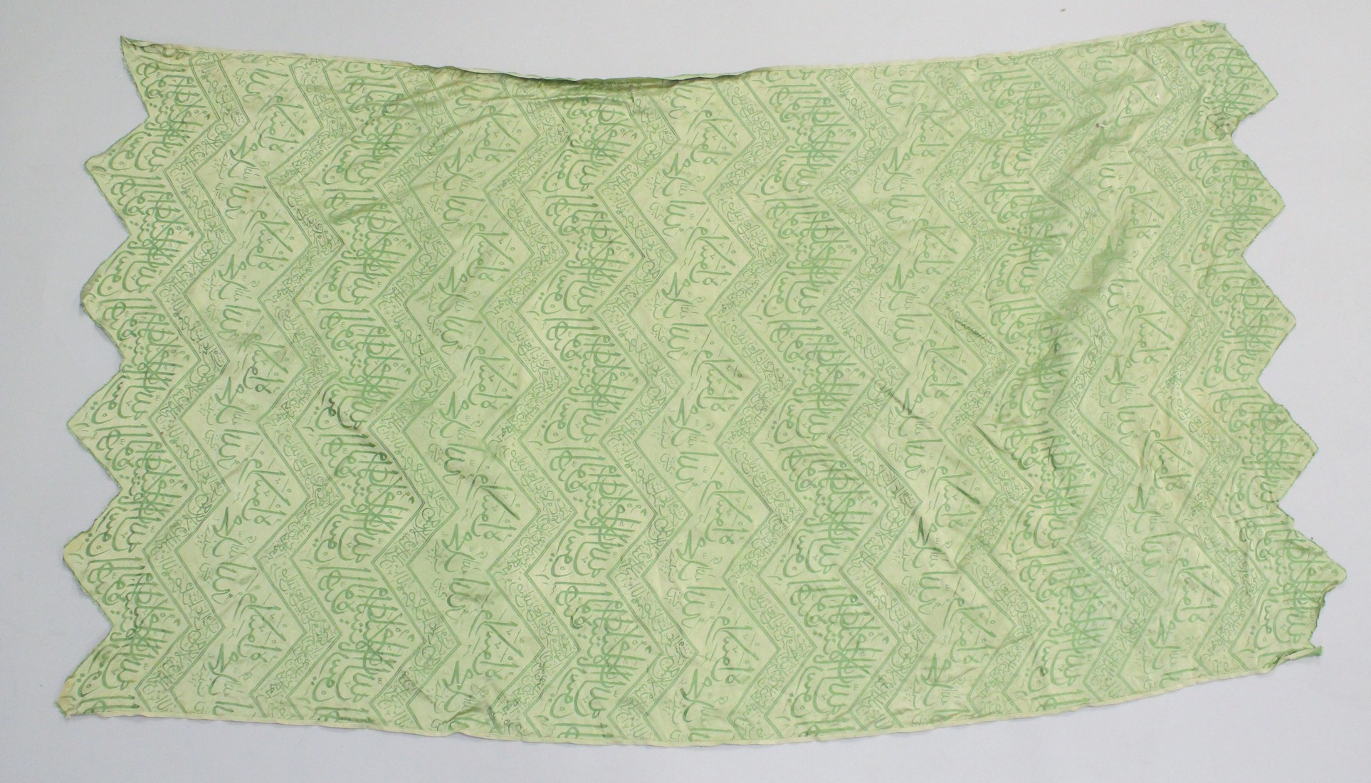 AN ISLAMIC GREEN SILK TEXTILE, embroidered with bands of calligraphy, 150cm x 85cm.