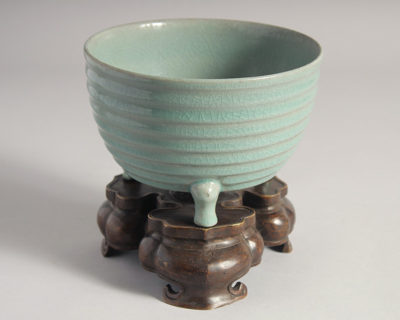 A CHINESE CELADON PORCELAIN TRIPOD CENSER with bronze stand, the base with carved characters. 15.5cm