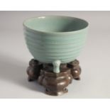 A CHINESE CELADON PORCELAIN TRIPOD CENSER with bronze stand, the base with carved characters. 15.5cm