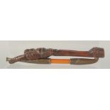 A JAPANESE METAL MOUNTED WOODEN TOBACCO PIPE with figural carved wood holder, pipe 20cm long.