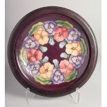 MOORCROFT PANSY DESIGN PLATE in an oak frame. 9.5ins diameter